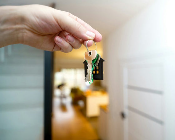 Een hand houdt een sleutelbos met een huisje als sleutelhanger omhoog in een lichte gang
