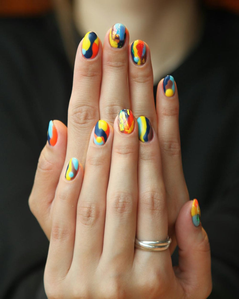 Twee handen met ovale nagels vol abstracte nail art in geel, oranje, blauw en rood