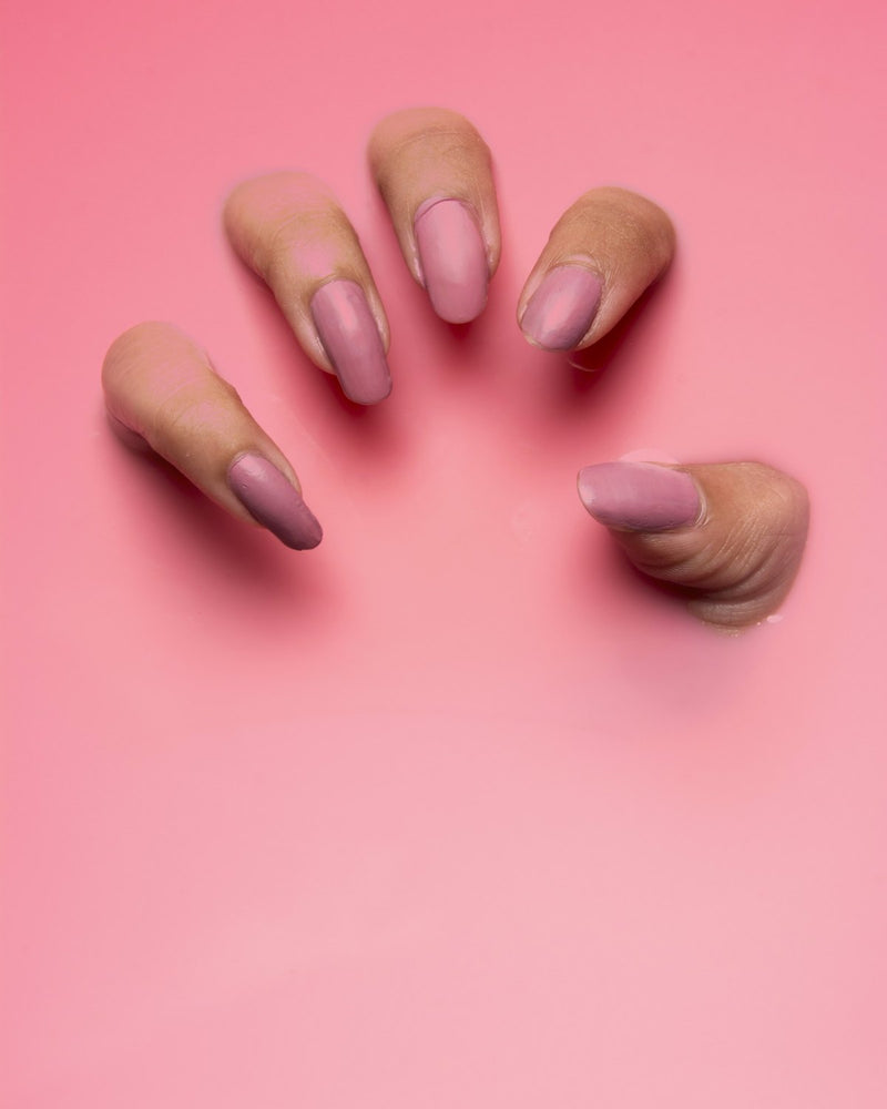 Vingers met matte oudroze nagels die door een roze vlak omhoog steken