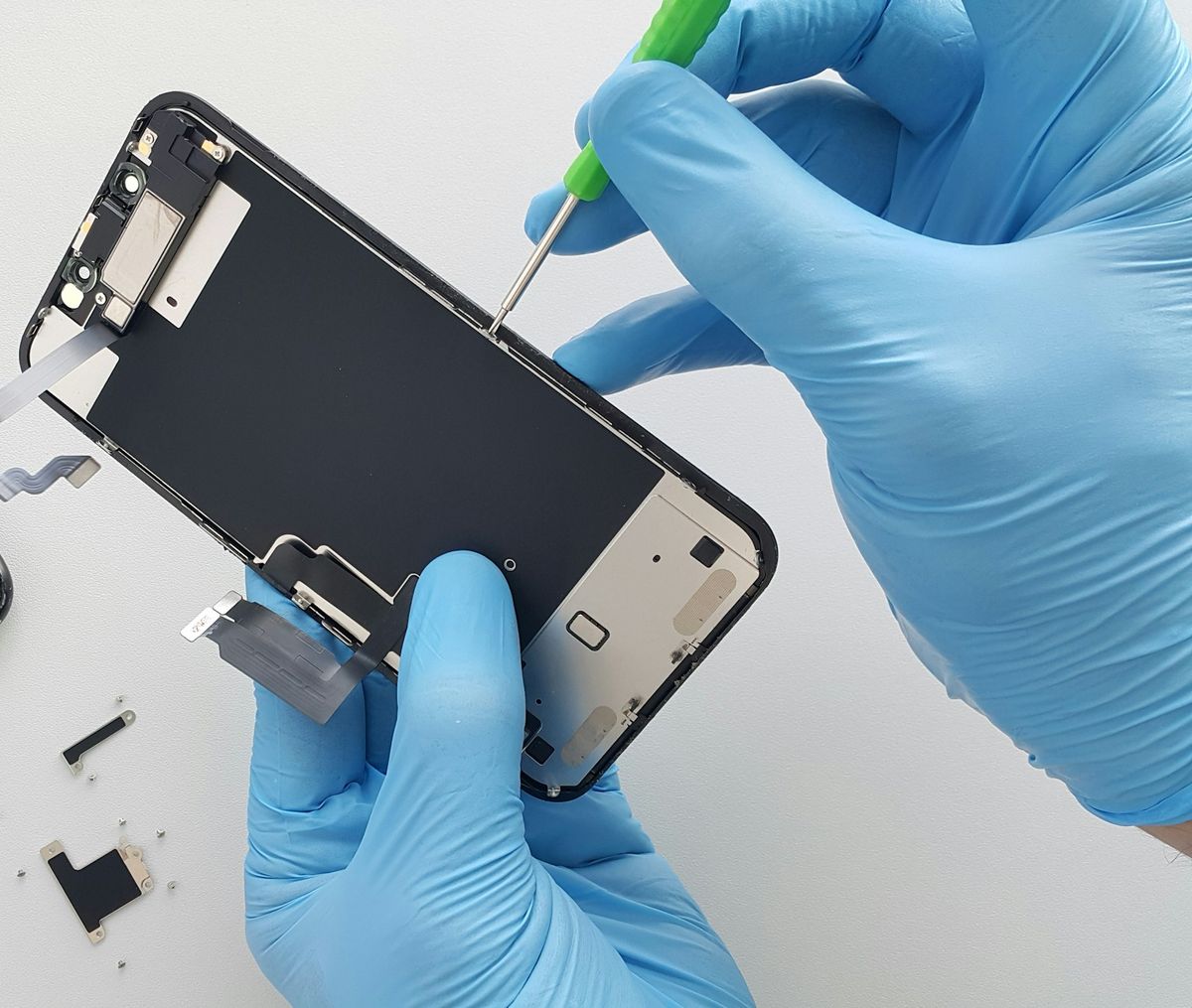 Handen in blauwe handschoenen tillen het scherm van een geopende telefoon op een witte werkplek