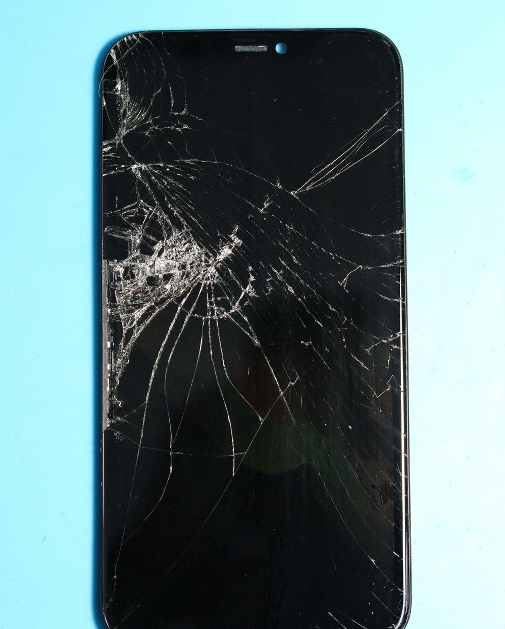 Een telefoon met een gebarsten scherm op een blauwe werkmat