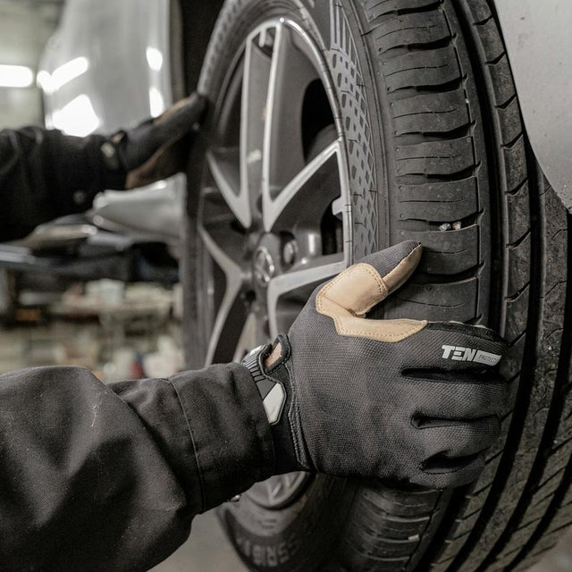 Monteur met handschoenen monteert een band op een auto