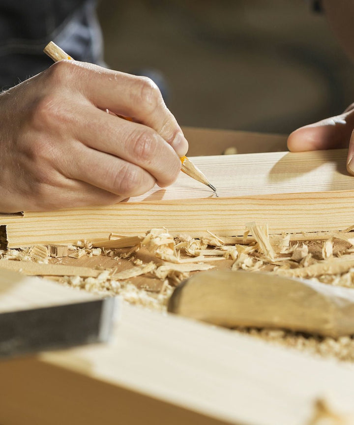 Handen tekenen met een potlood een maat af op een houten balk