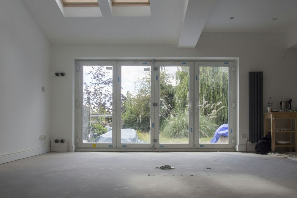 Na: lichte leefruimte met strak stucwerk, dakramen en een harmonicapui naar de tuin