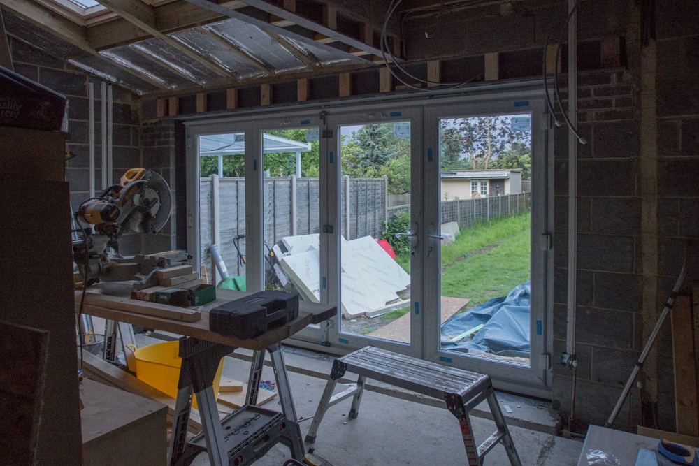 Tijdens: ruwbouw met kale muren, gereedschap en de nieuwe pui