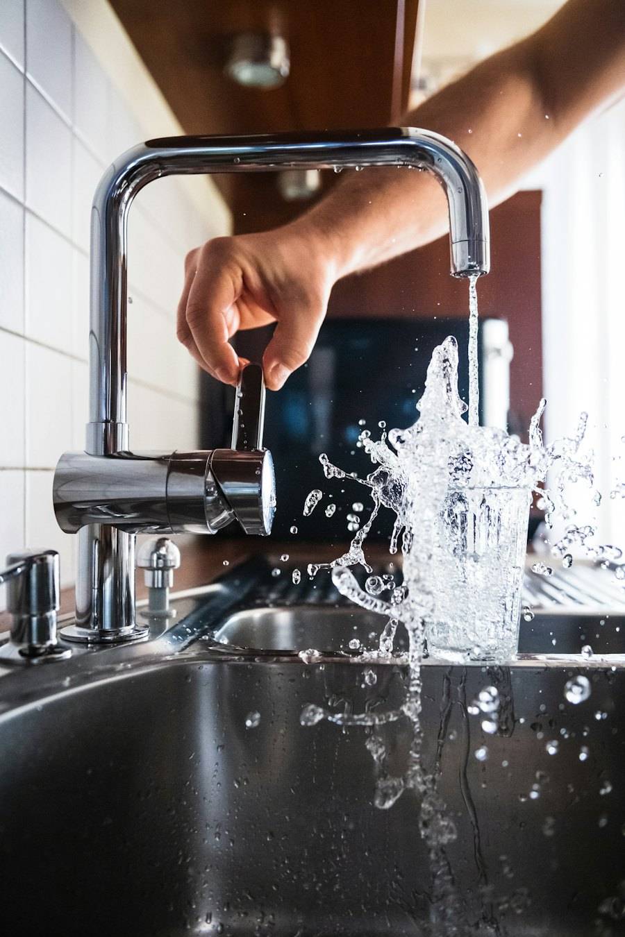 Een hand zet een chromen keukenkraan open, het water spat in de spoelbak