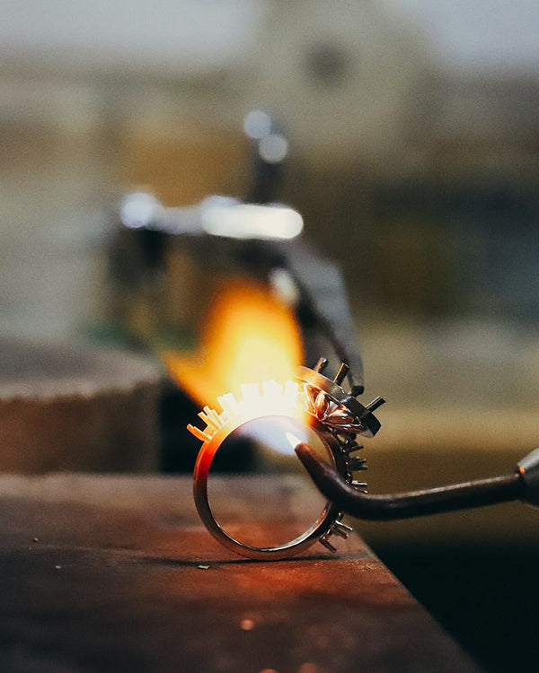 Een fijne vlam soldeert een ring die vastzit in een derde hand op de werkbank