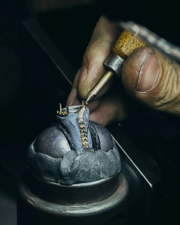 Een goudsmid zet met een graveerstift kleine stenen in een ring die vastzit in zetwas