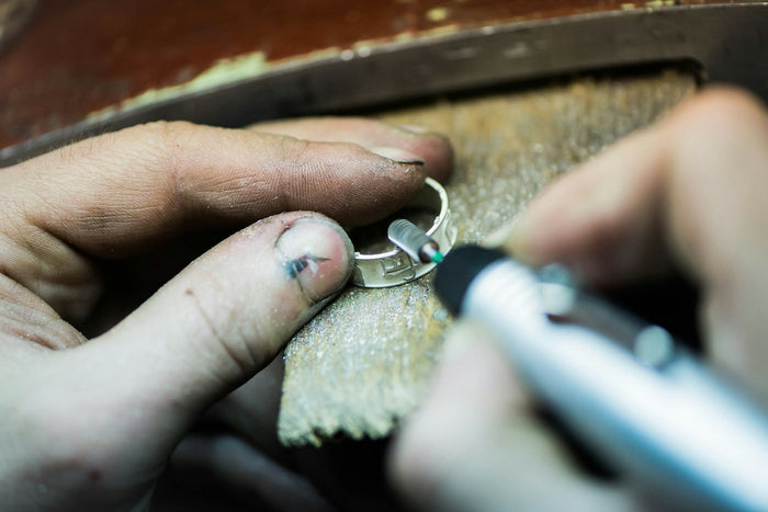 Handen van een goudsmid polijsten een zilveren ring op de werkbank met een klein slijpapparaat
