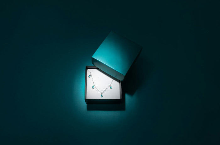 Een open cadeaudoosje met een sieraad erin, in blauwgroen licht
