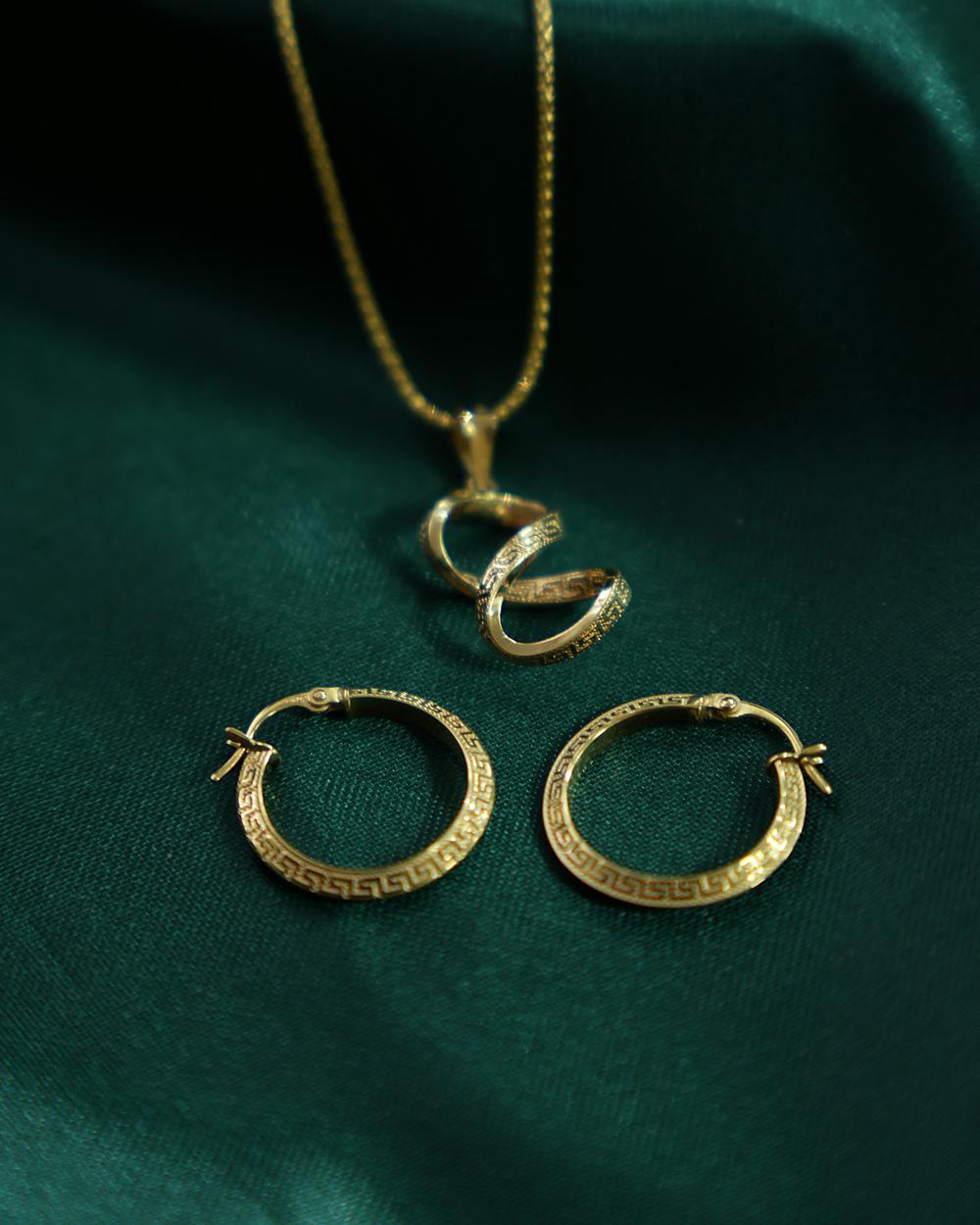 Een gouden hanger in de vorm van een krullende slang aan een fijne ketting, met twee gouden creolen op groene zijde