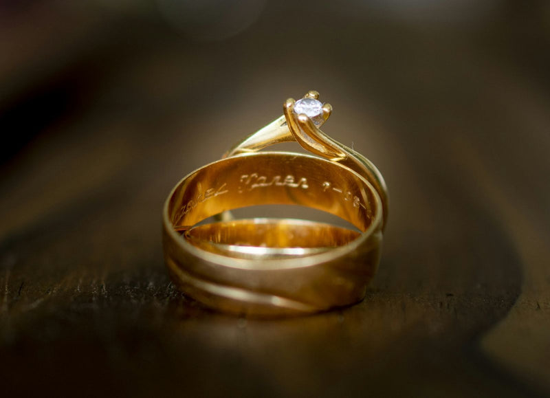 Een gouden trouwring met een gravure aan de binnenkant, naast een verlovingsring met een diamant