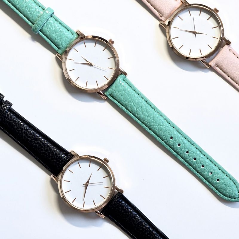 Drie horloges met een witte wijzerplaat en leren banden in mint, lichtroze en zwart
