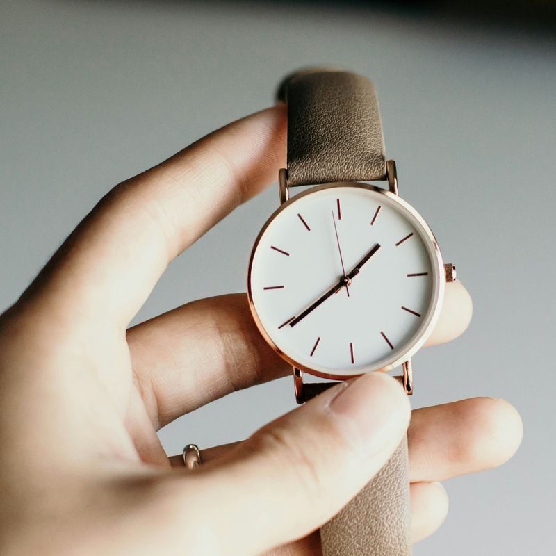 Een hand houdt een horloge vast met een witte wijzerplaat, een roségoudkleurige kast en een taupe leren band