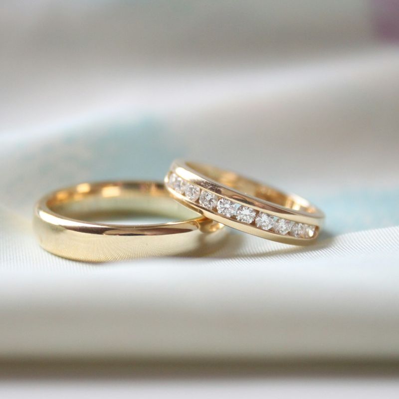 Een gladde gouden trouwring naast een smallere gouden ring met een rij diamanten