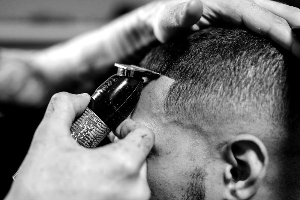 Close-up van een trimmer langs de slaap, de kapper houdt het hoofd vast