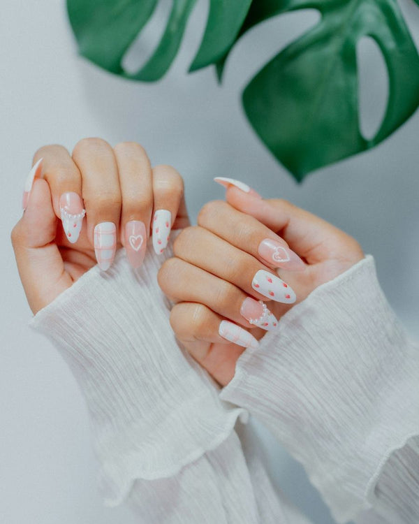 Lichtroze amandelnagels met kleine hartjes, naast een monsterablad
