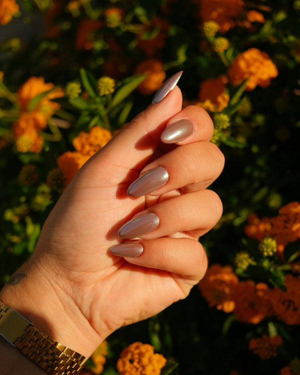 Amandelnagels met een mokkakleurige chrome glans tegen oranje bloemen