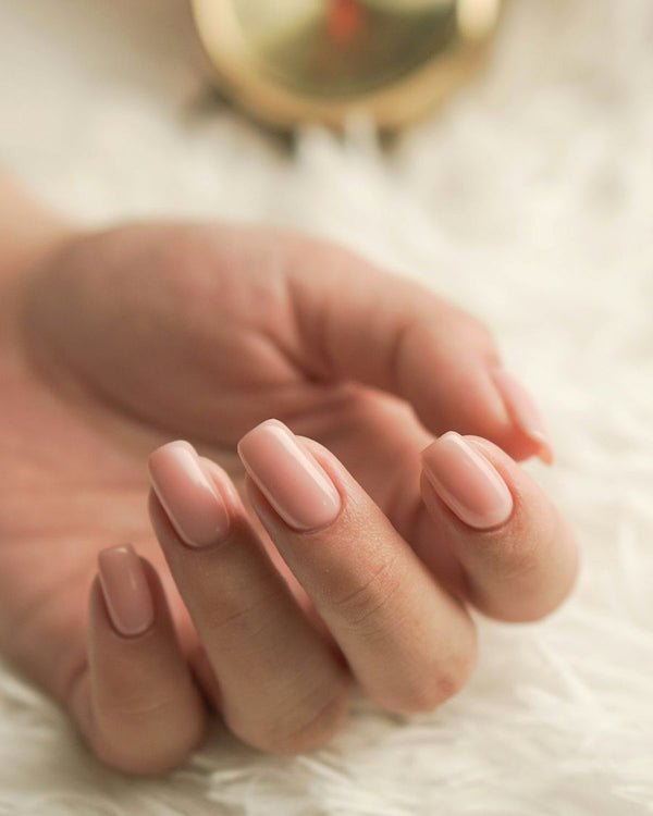 Hand met korte, glanzende nude nagels op een zacht wit vachtje