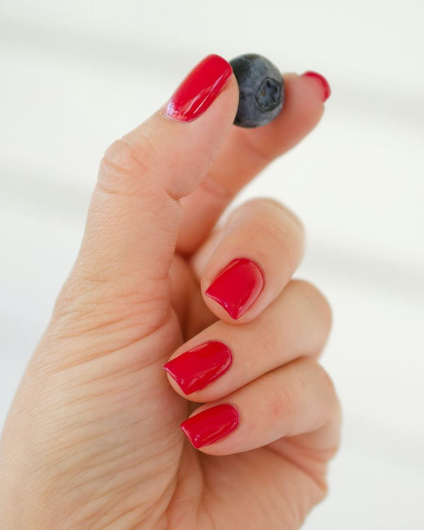 Hand met korte knalrode nagels die een bosbes vasthoudt