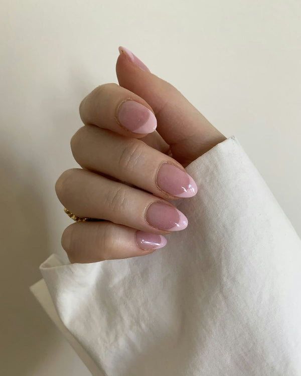 Hand met ovale lichtroze nagels tegen een witte doek