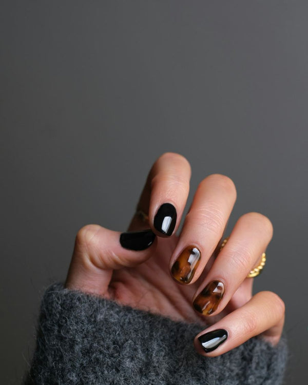 Nagels met zwarte lak en een schildpadpatroon, hand in een grijze trui