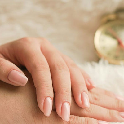 Handen met nude amandelnagels op een wit vachtje