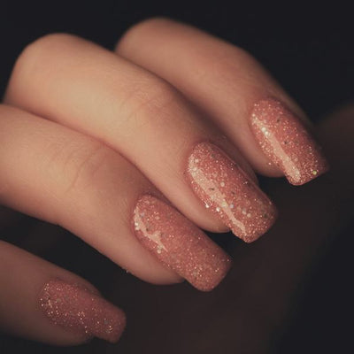 Nagels met roségouden glitter tegen een donkere achtergrond