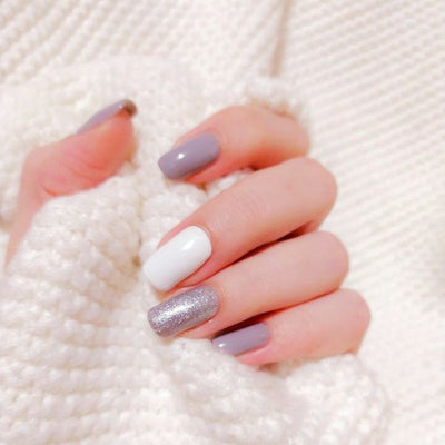 Nagels in lila, wit en zilverglitter tegen een witte trui