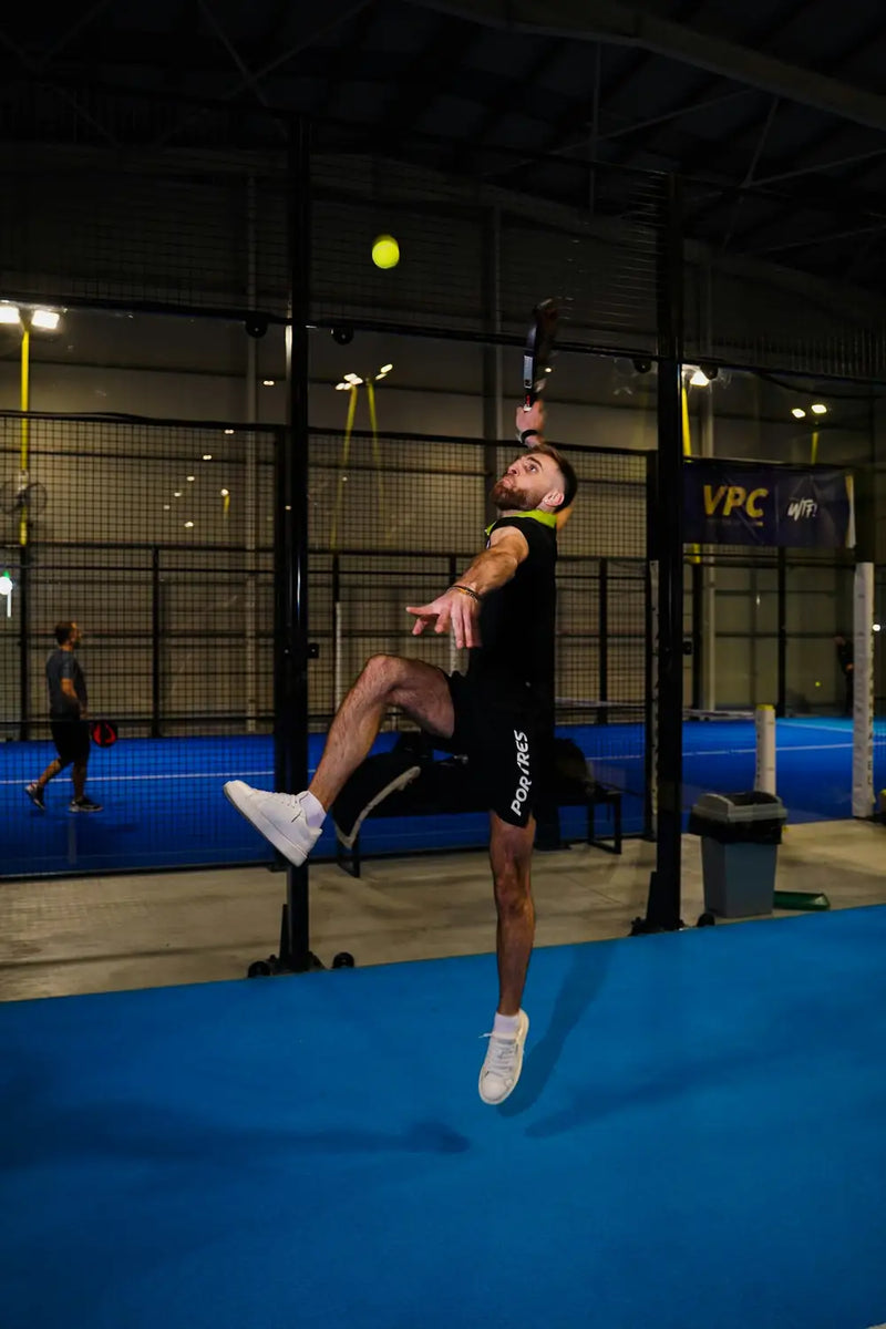 Een speler slaat een smash in een binnenhal met blauwe padelbanen