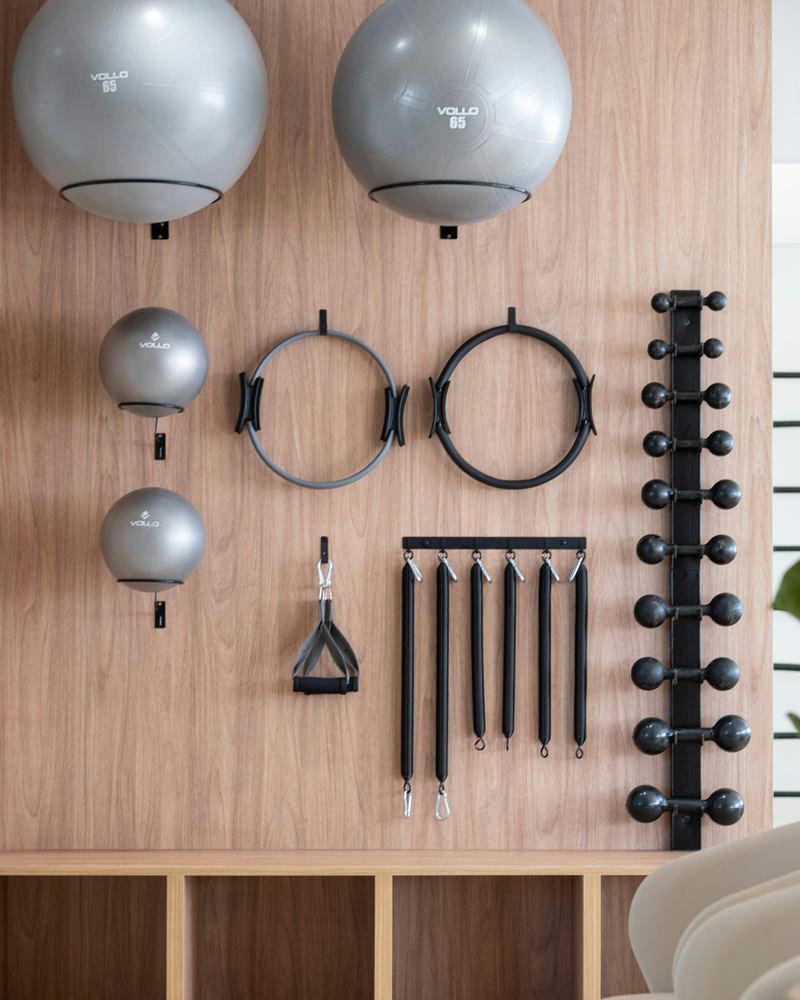 Een houten wand met pilatesballen, twee ringen, weerstandsbanden en kleine gewichten, netjes opgehangen