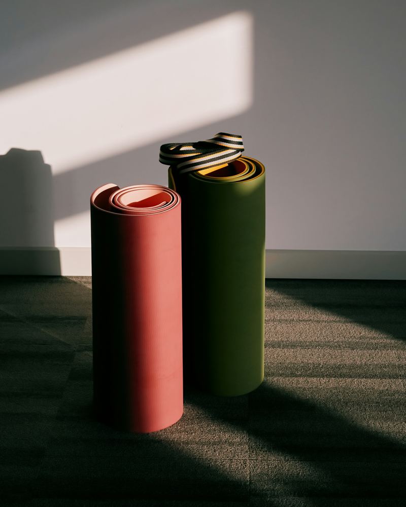 Twee opgerolde matten, een terracotta en een olijfgroene, in het late zonlicht tegen een witte muur
