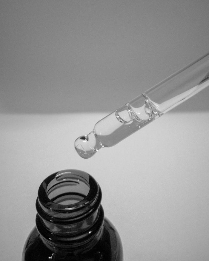 Pipet met een heldere druppel serum boven een donker glazen flesje