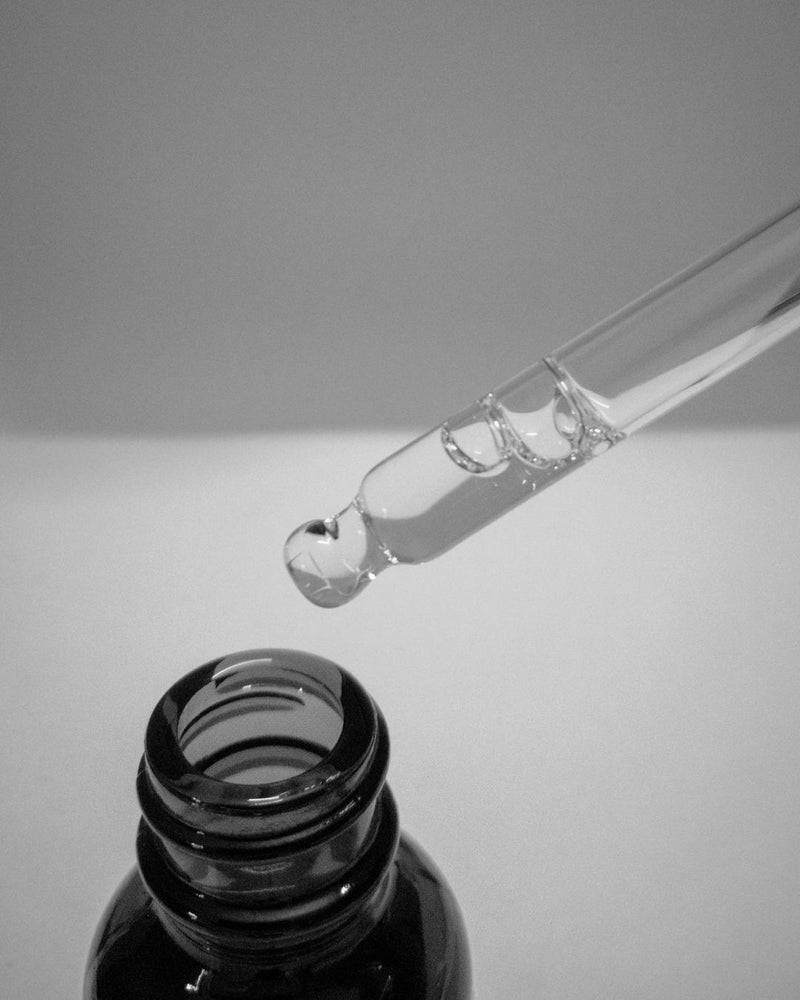 Pipet met een heldere druppel serum boven een donker glazen flesje