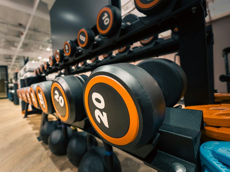 Een rek met dumbbells van 10 en 20 kilo, met oranje randen, in een lichte sportschool