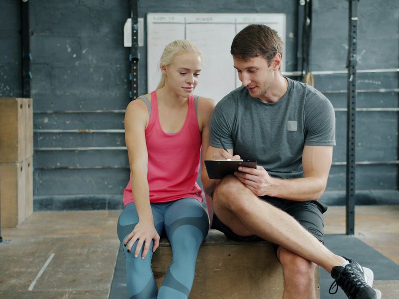 Een trainer bespreekt een trainingsschema met een sporter, ze zitten samen op een houten box