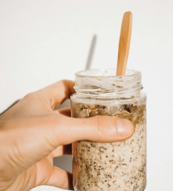 Hand houdt een pot overnight oats met een houten lepel vast