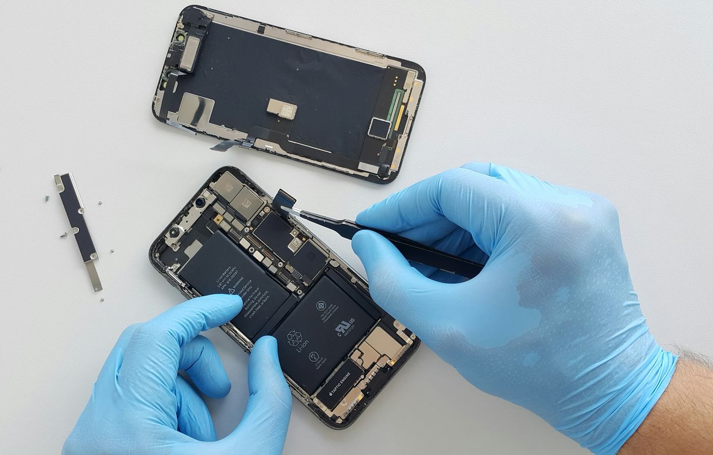 Handen in handschoenen koppelen met een pincet de batterij los van een geopende telefoon